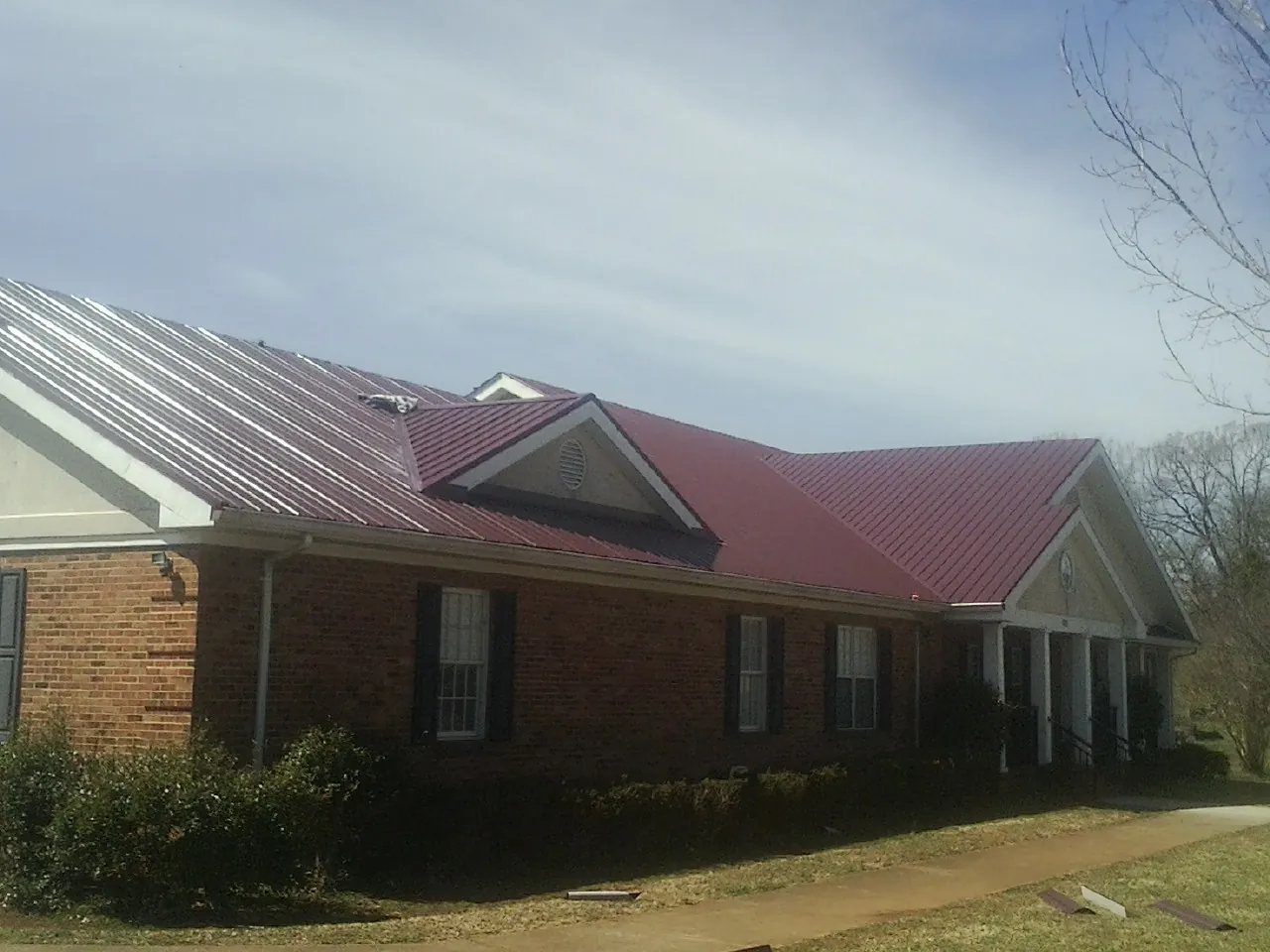 Red metal roof with gabled entries on a long brick building, from a Hail Damage Roof Repair job in Lompoc