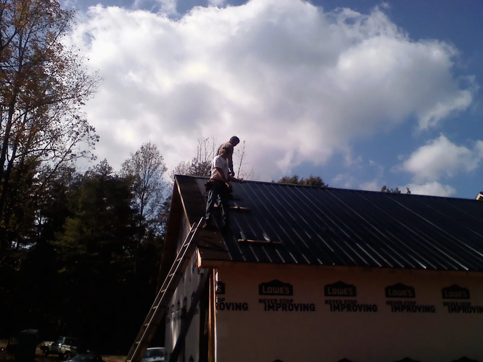 Roofer fastening dark metal panels high against a cloudy sky, from a Roof Inspection job in Lompoc
